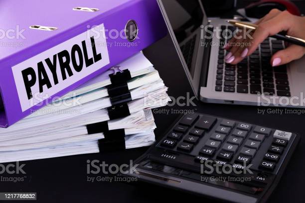 Text, word Payroll is written on a folder lying on documents on an office desk with a laptop and a calculator. Business concept.